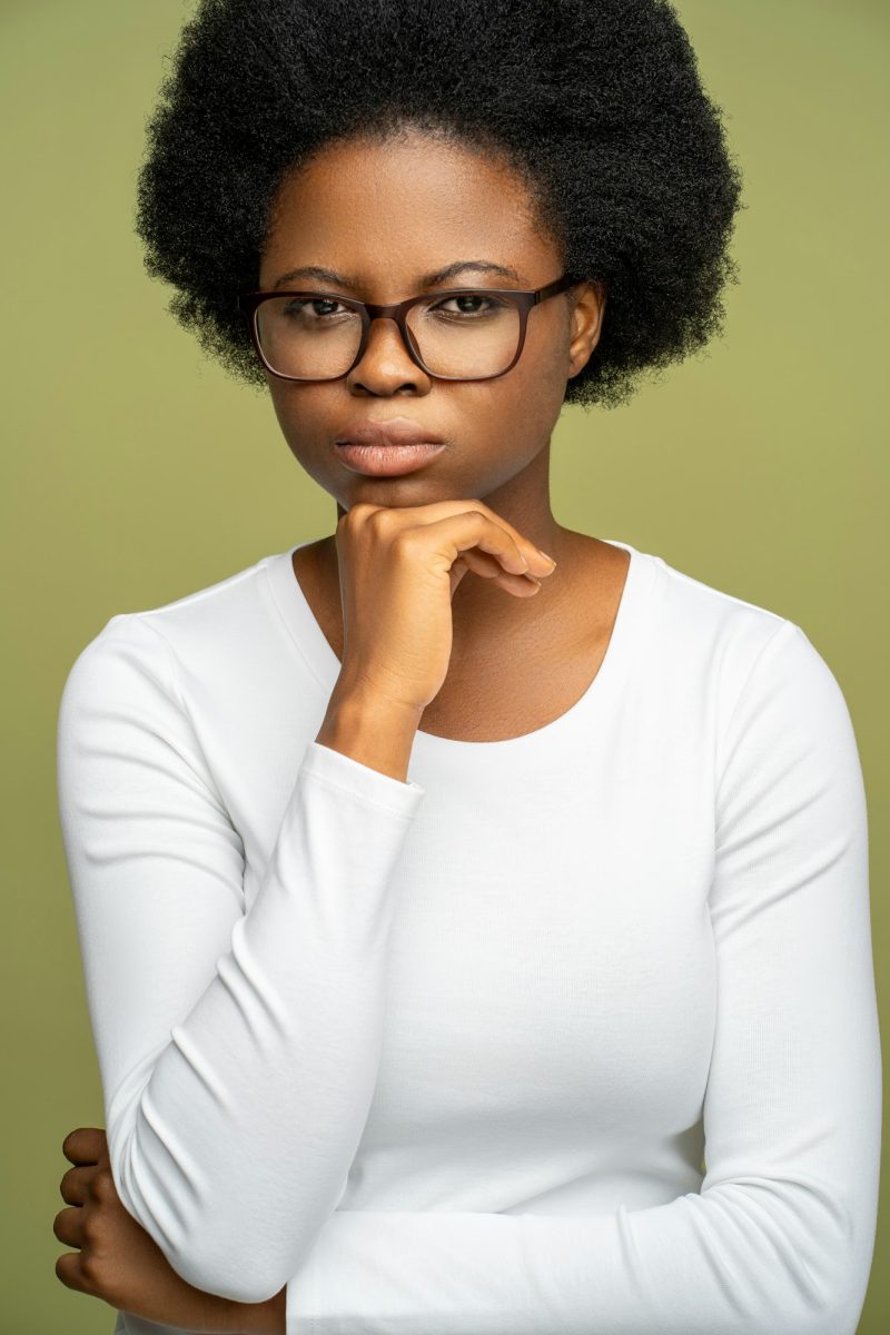 Self assured intelligent African American woman in glasses looking at camera with strict glance.