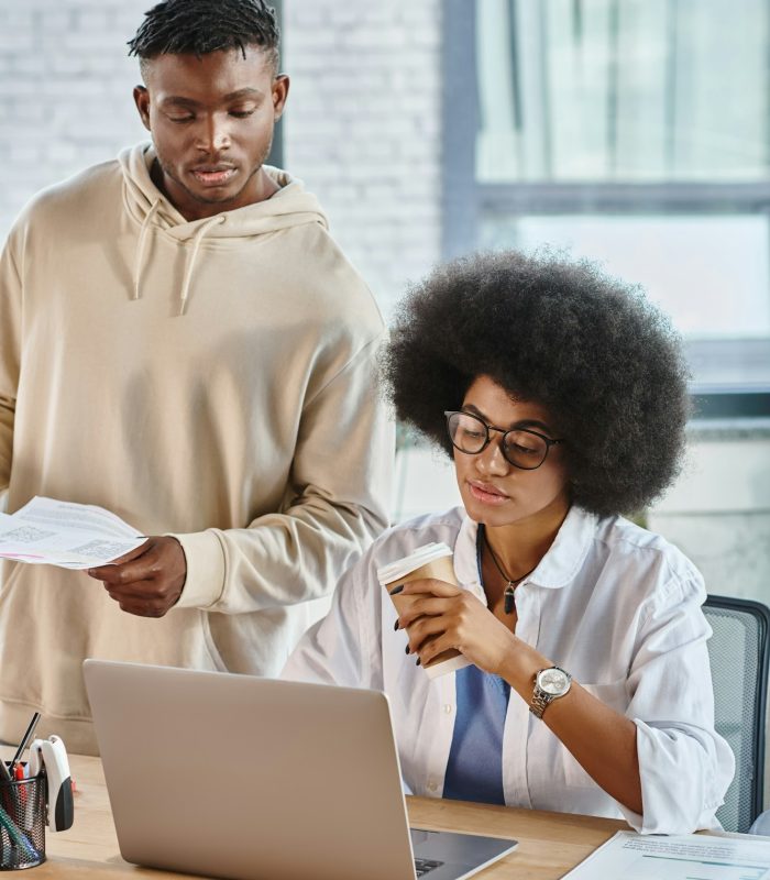 african american colleagues working hard with laptop and papers with coffee in hand, business